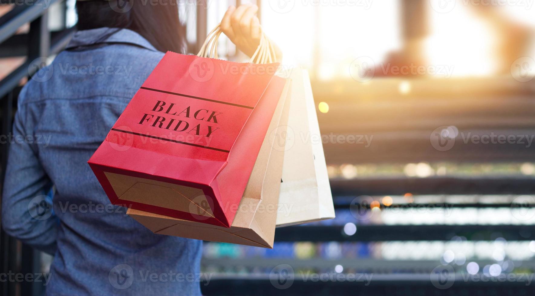 vista trasera de una mujer sosteniendo una bolsa de compras del viernes negro mientras sube las escaleras al aire libre en el fondo del centro comercial foto