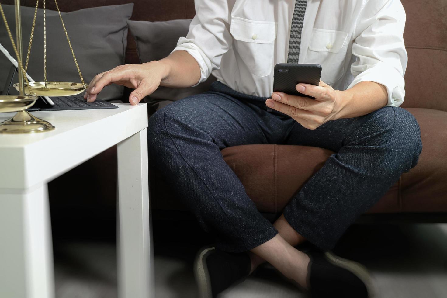 Justice and Law context.Male lawyer hand sitting on sofa and working with smart phone,digital tablet computer docking keyboard with gavel and document on living table at home photo