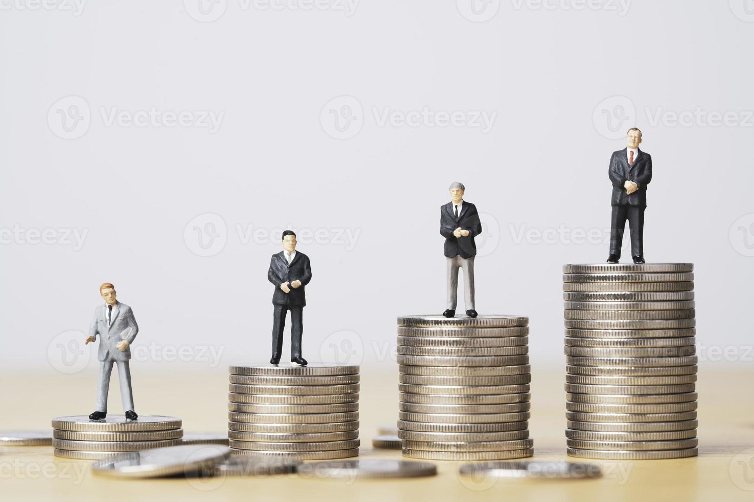 diferentes empresarios en miniatura parados en monedas de diferentes alturas apiladas, desigualdad de ingresos y salario en cada posición en el concepto de empresa. foto