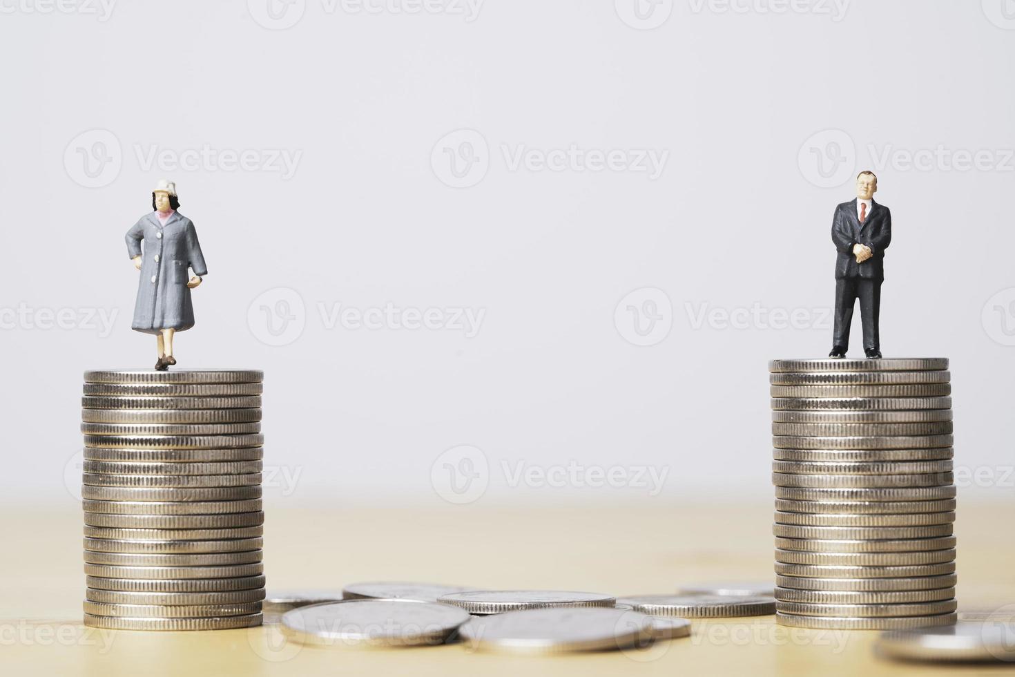 figura en miniatura de un hombre de negocios parado en monedas iguales apiladas de una mujer de negocios por la igualdad de género masculino y femenino del concepto de ingresos y salarios. foto