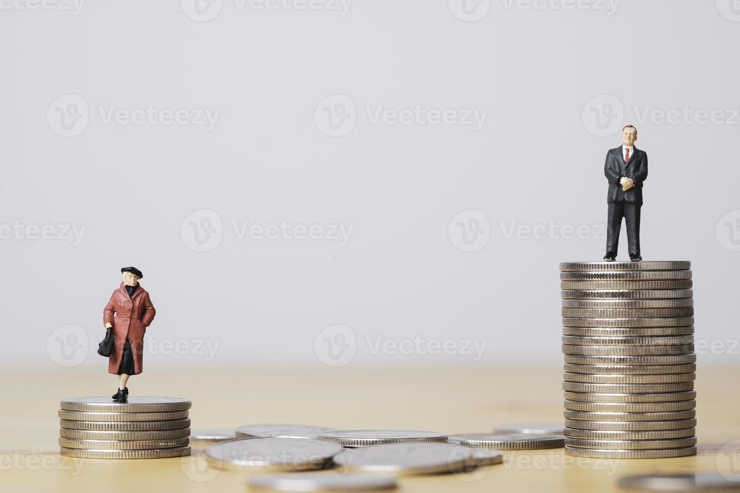 figura en miniatura de un hombre de negocios de pie sobre un apilamiento de monedas más alto que una mujer de negocios por la desigualdad de género masculino y femenino del concepto de ingresos y salarios. foto