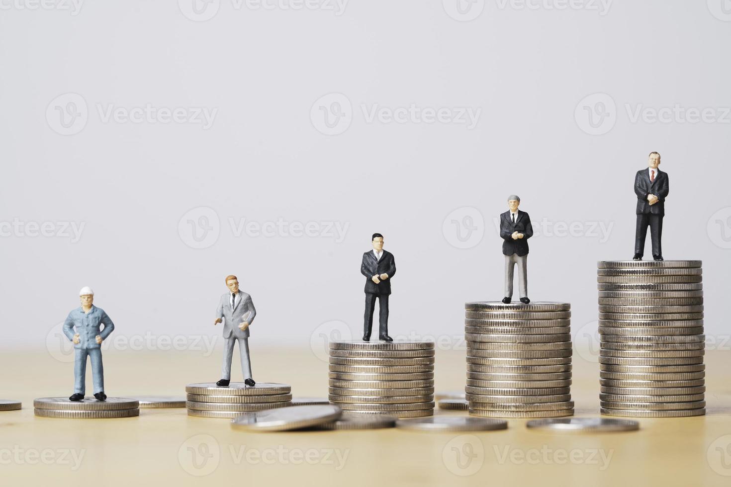 Different miniature businessman standing on different height coins stacking , Inequality income and salary in each position in company concept. photo