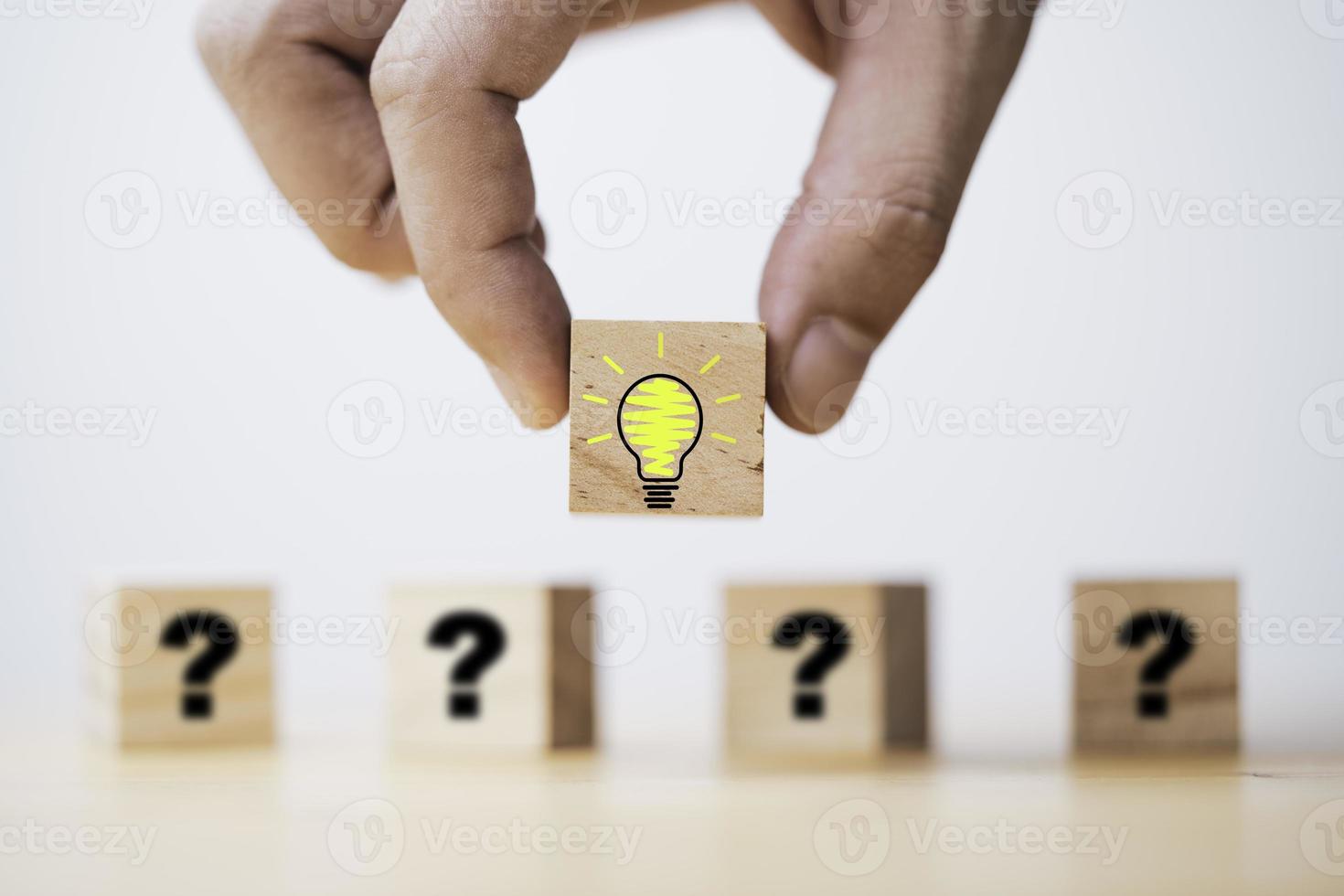 Hand putting lightbulb on wooden cube block in front of question mark for question and answer concept. photo