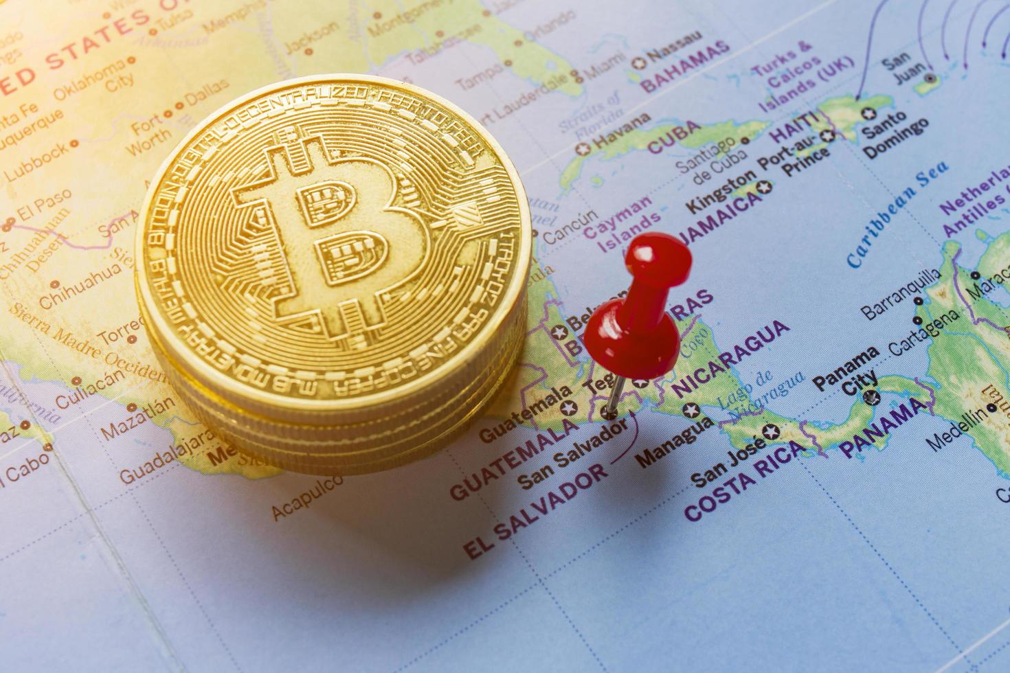 A red pin is pinned on the world map of El Salvador and there is a bitcoin next to it. photo