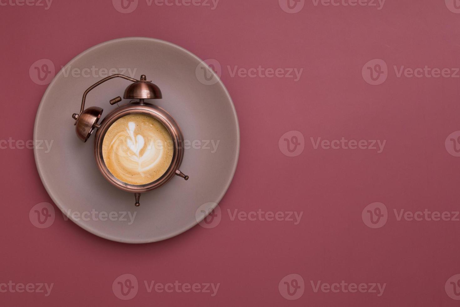 Alarm clock on a plate with frothy coffee and a pattern. Morning rise with coffee for breakfast concept. Copy space photo