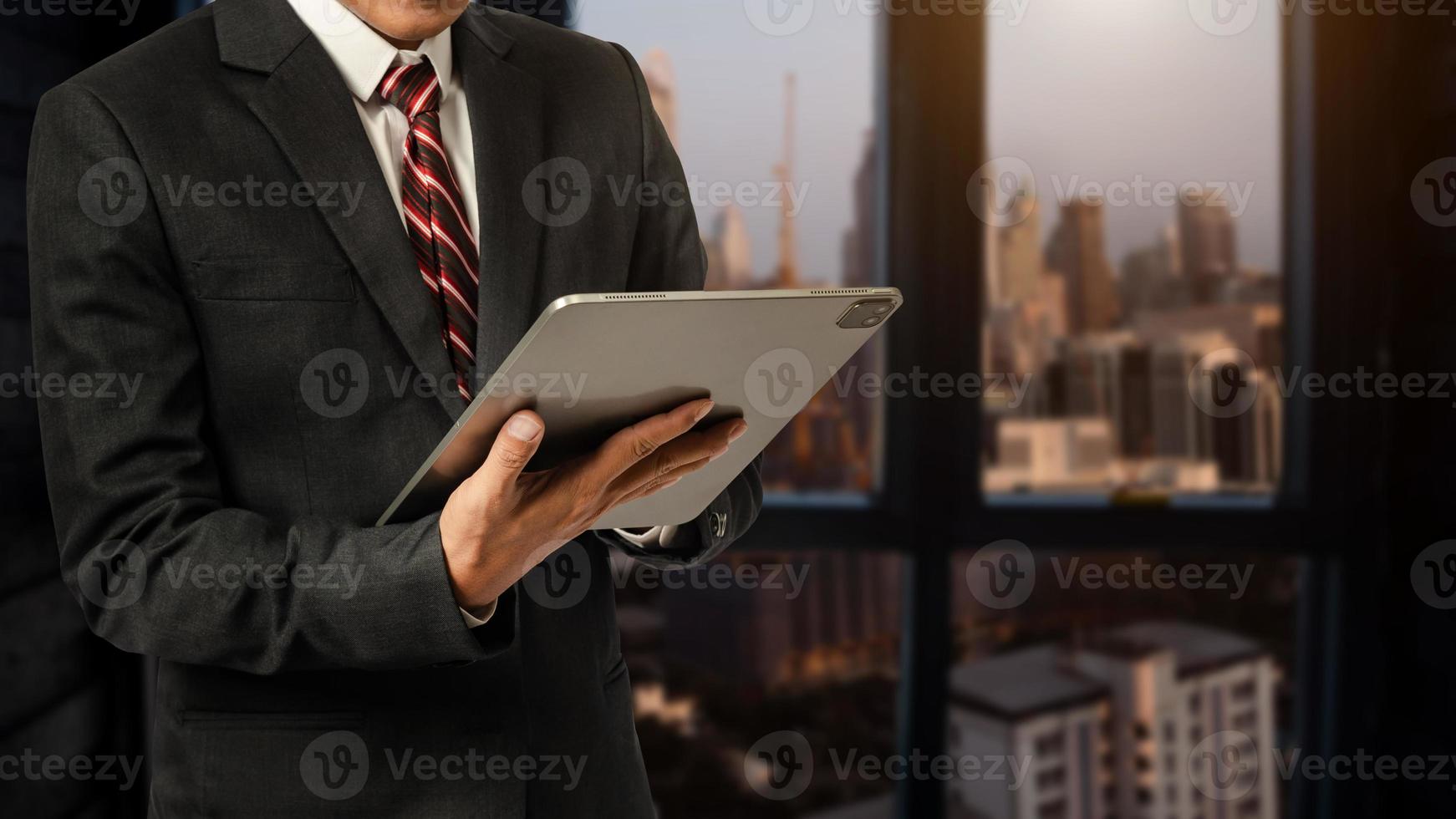 Business man in white shirt using or browsing internet on digital tablet computer with blurred modern office background photo