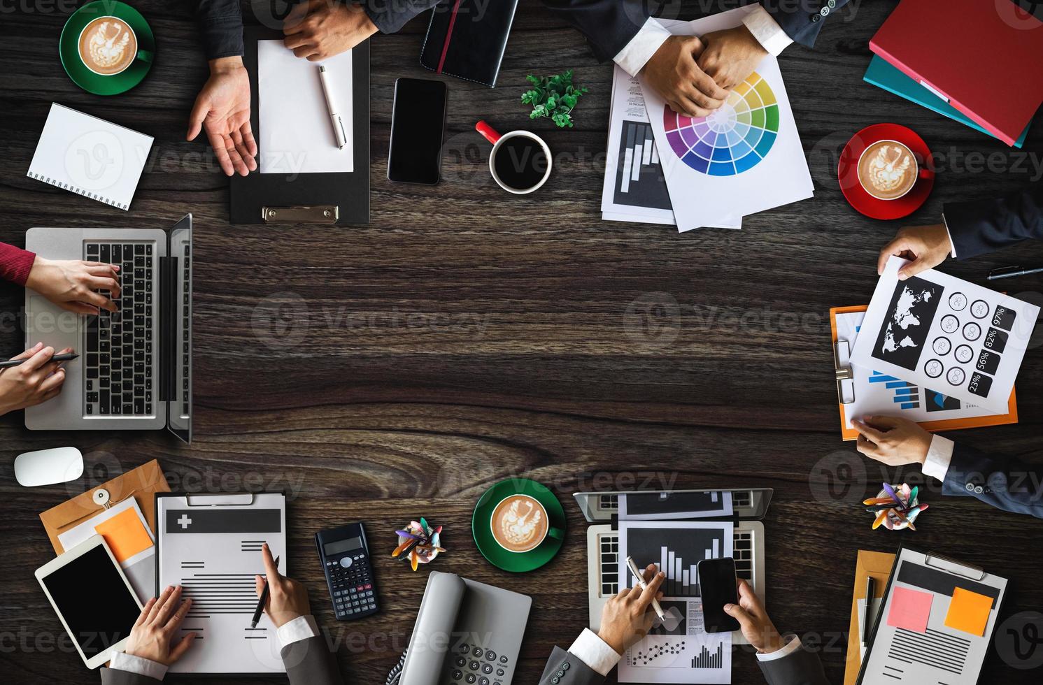 vista superior del grupo empresarial de personas ocupadas multiétnicas que se reúnen con otros en una oficina moderna con computadora portátil, teléfono inteligente, tableta, café y documento en la mesa. foto