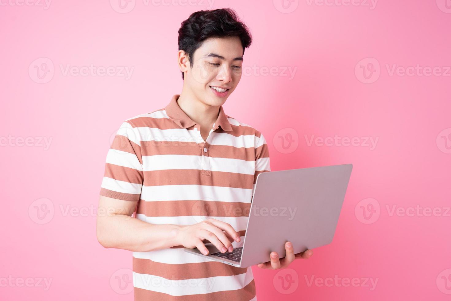 Portrait of young Asian man using laptop on pink background photo