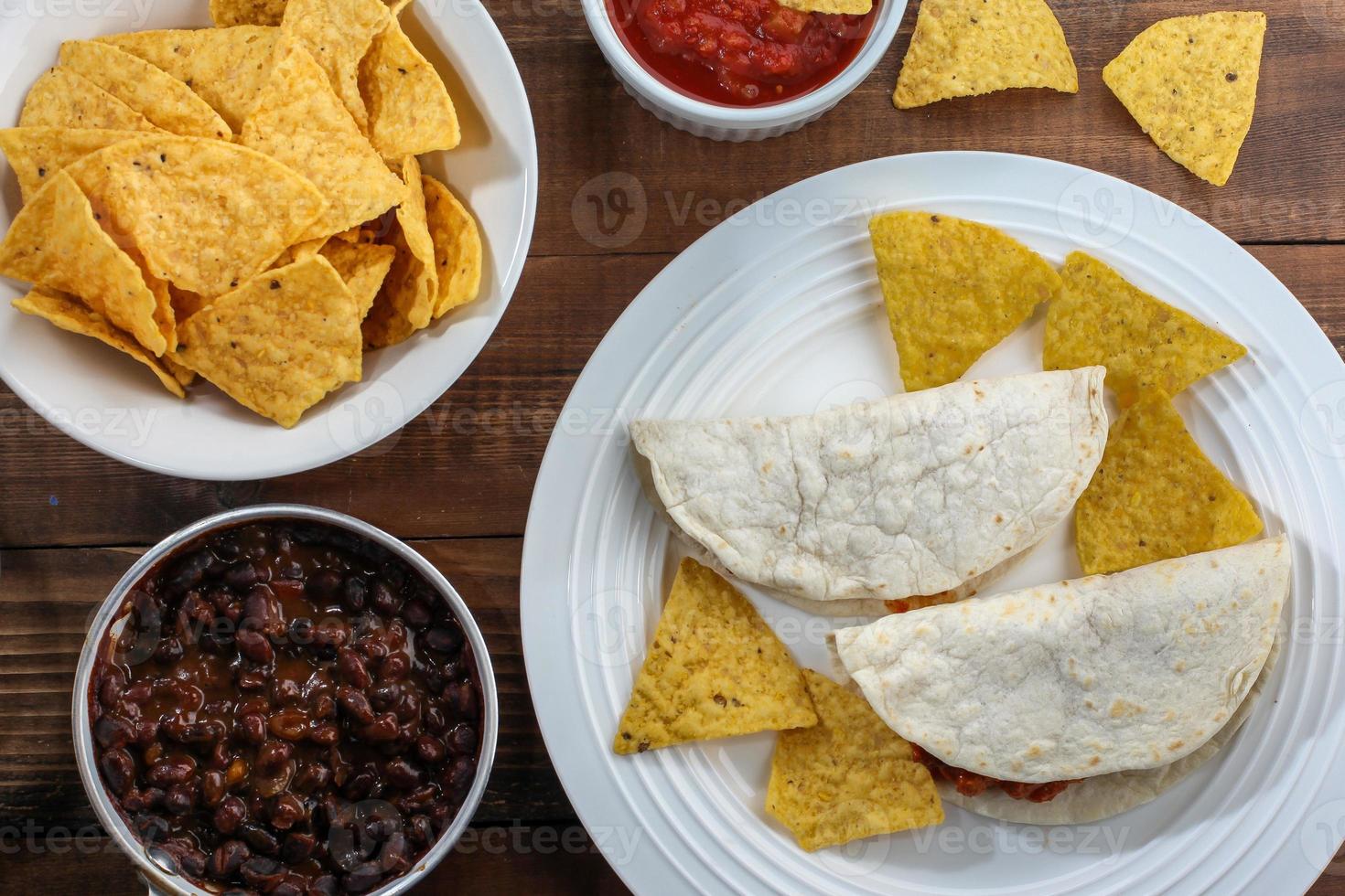 Tortilla and chips inside bowl with salsa and beans on rustic wooden table top view photo