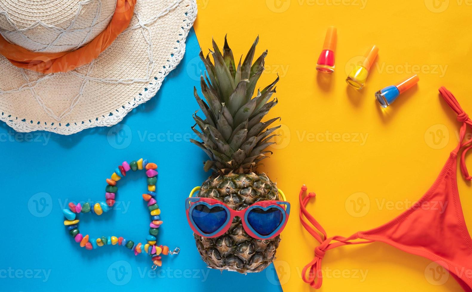 Summer composition. Pineapple in sunglasses, hat, beads and nail polishes on a yellow background with copy space. Vacation concept. Flat lay. photo