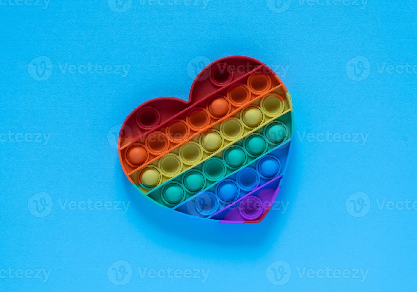 color pop it juguete antiestrés para niños. Arco iris en forma de corazón aislado sobre fondo azul. foto