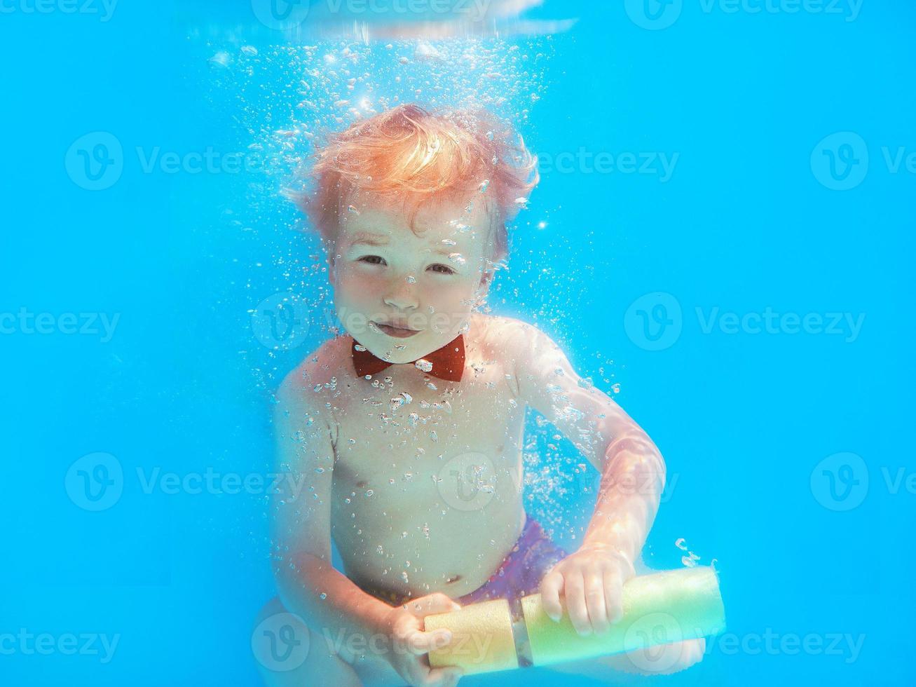 niño pequeño con mariposa roja buceando bajo el agua en la piscina, aprende a nadar. concepto de deporte y vacaciones foto