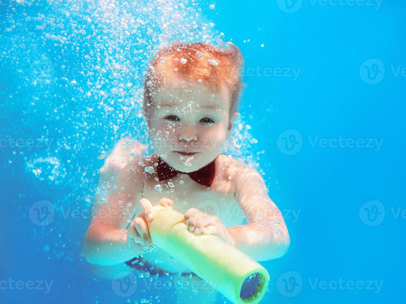 niño pequeño con mariposa roja buceando bajo el agua en la piscina, aprende a nadar. concepto de deporte y vacaciones foto