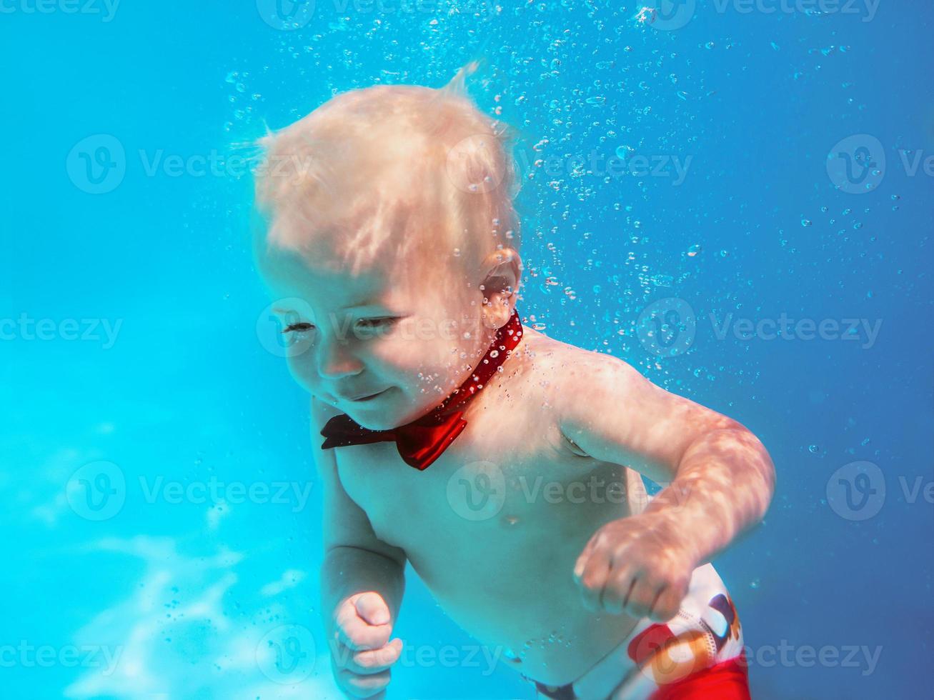 Little boy infant with red butterfly diving underwater in swimming pool, learn to swim. Sport and vacation concept photo