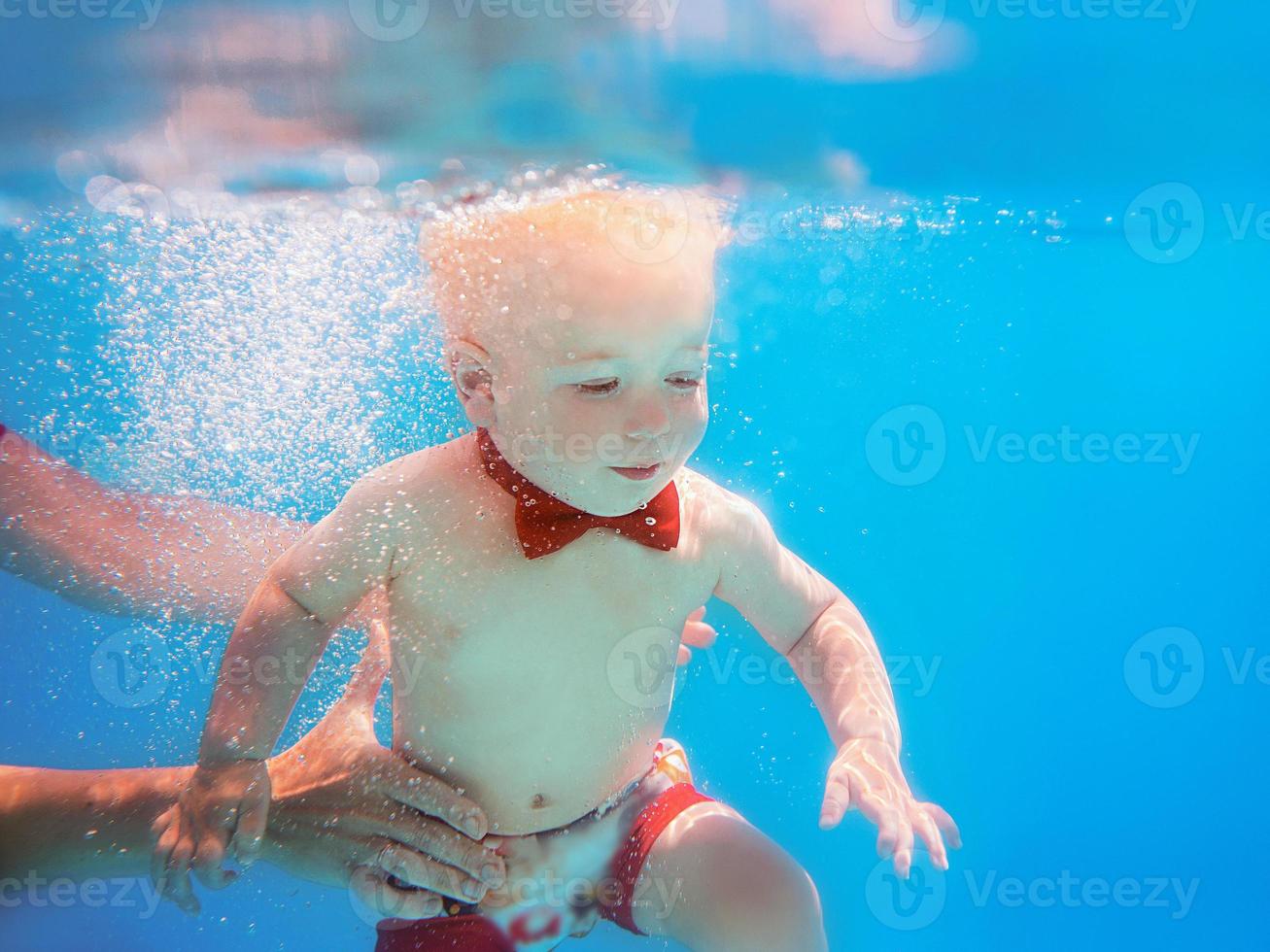 Little boy infant with red butterfly diving underwater in swimming pool, learn to swim. Sport and vacation concept photo