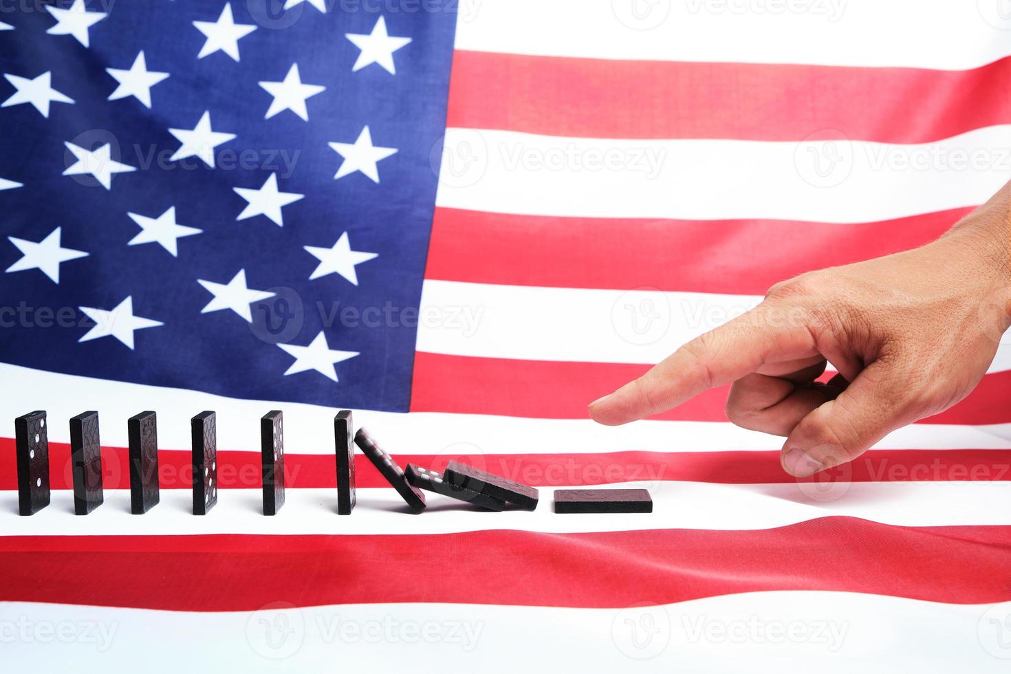 White man's finger pushing a Domino causing a chain reaction against background of the us flag. photo