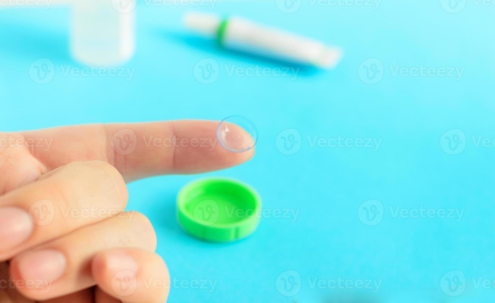 Contact lens on finger on light blue background.Eye care products in the background, space for text ,top view. photo