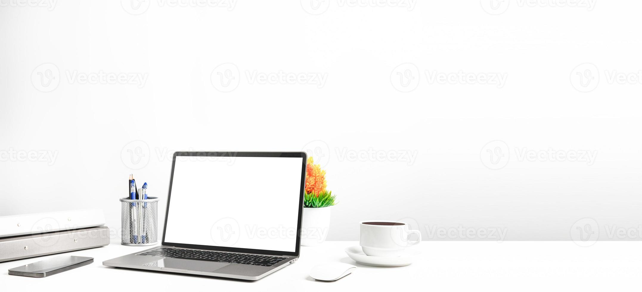 Blank white screen laptop on a white table in the office. Working concept using technology smartphones, notebook, coffee cup. Copy space on right for design or text, Closeup, Gray, and blur background photo