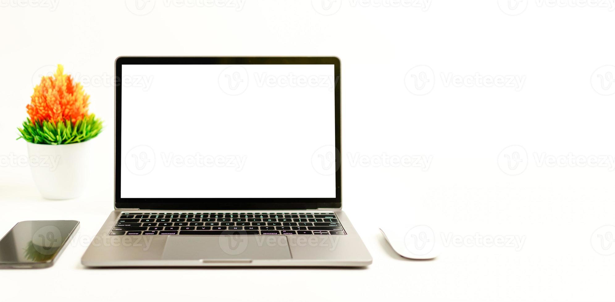 Blank white screen laptop on a white table in the office. Working concept using technology smartphones, notebook, internet. Copy space on right for design or text, Closeup, Gray, and blur background photo