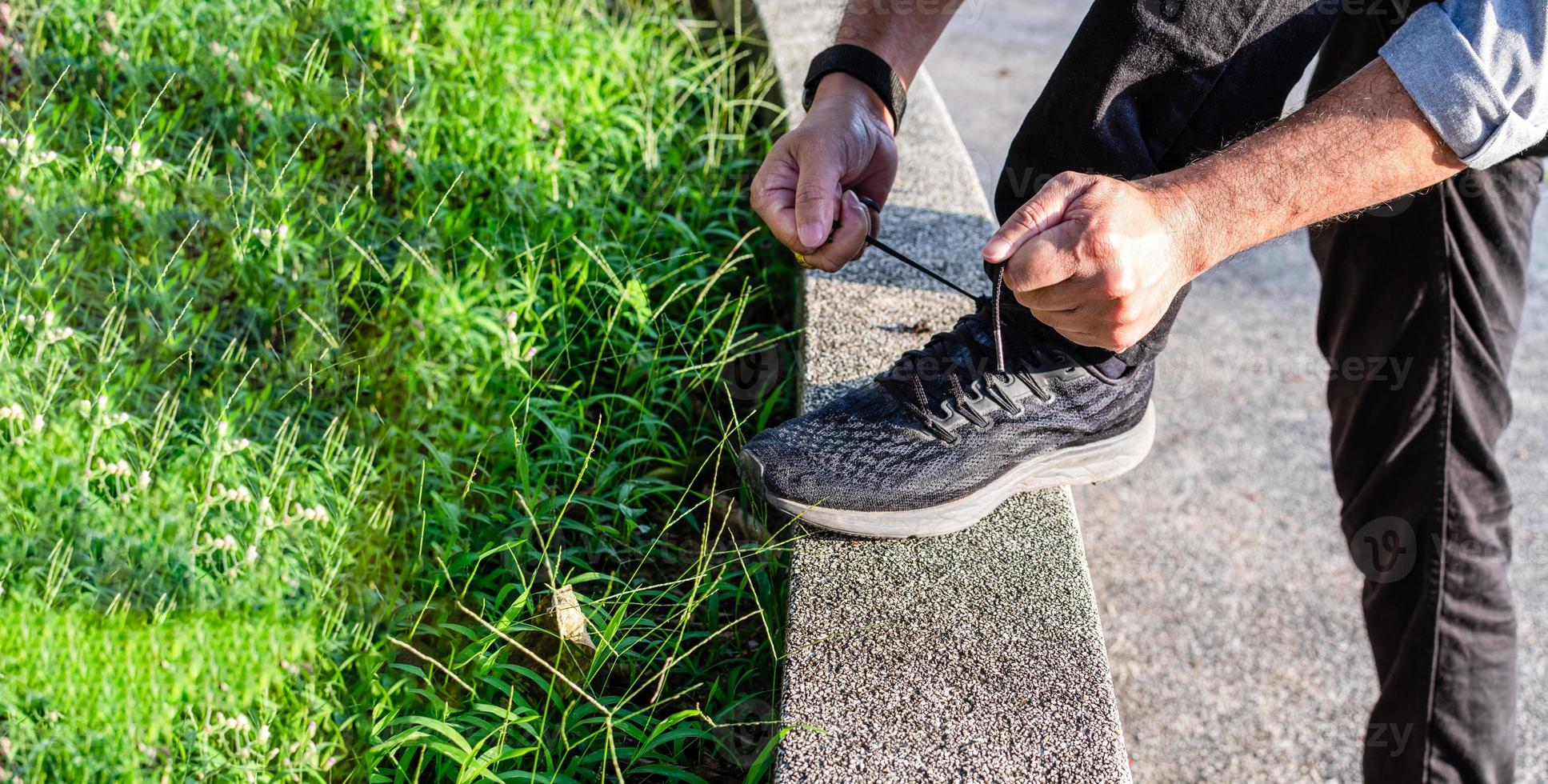 A man wears jeans tying black shoelaces in the sunlight on a sunny day in the park. selective focus, Closeup, Copy space, Blurred background photo