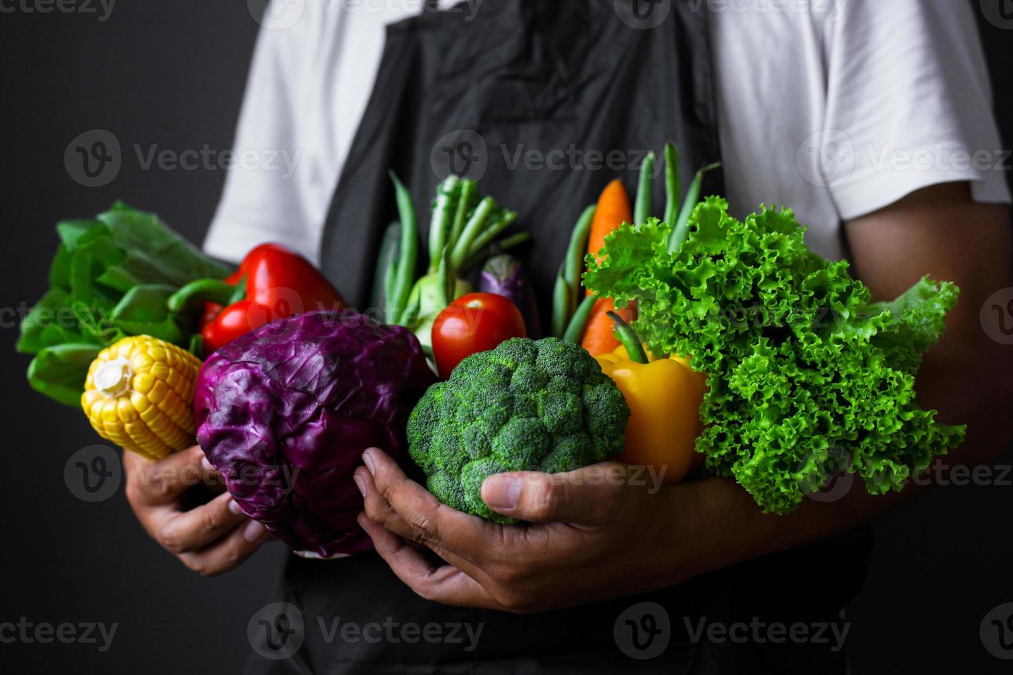 Man wearing apron holding various vegetables in both hands photo