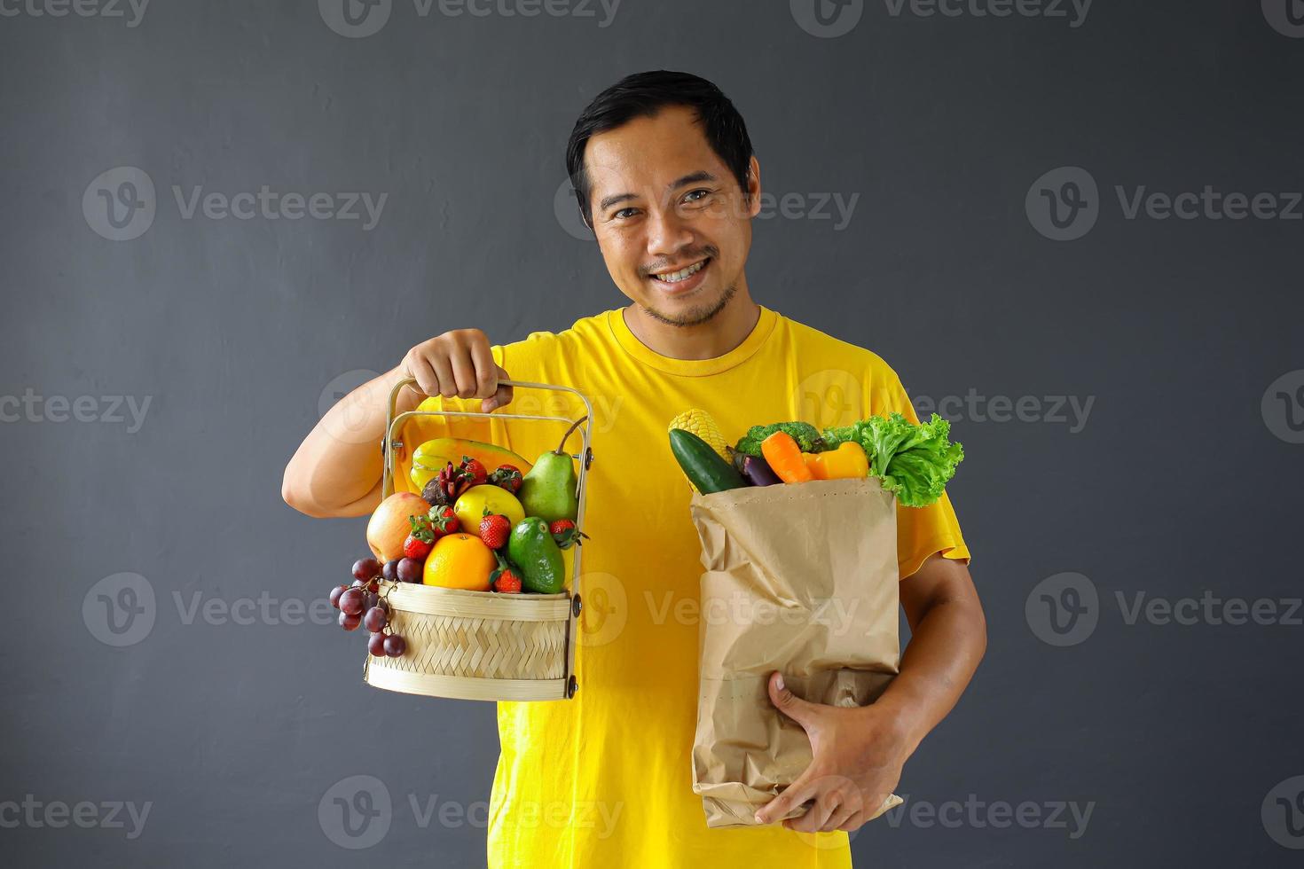 hombre asiático sosteniendo una cesta de frutas y verduras en una bolsa de compras para un concepto de estilo de vida saludable foto