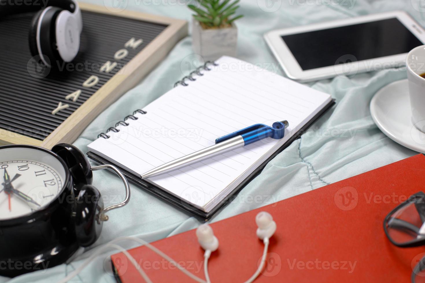 Monday flat lay concept top side view with blank notebook and pen, multimedia accessories, book and glasses, alarm clock, flowers and coffee on white background photo