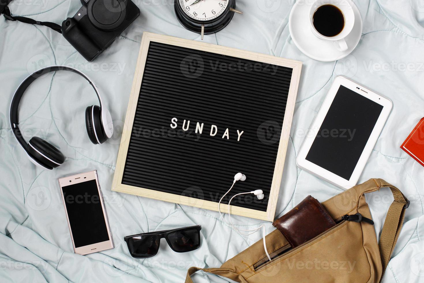 concepto plano de domingo con accesorios de entretenimiento multimedia, gafas de sol, reloj despertador, gadget, cámara, auriculares y café para refrescarse sobre fondo blanco foto