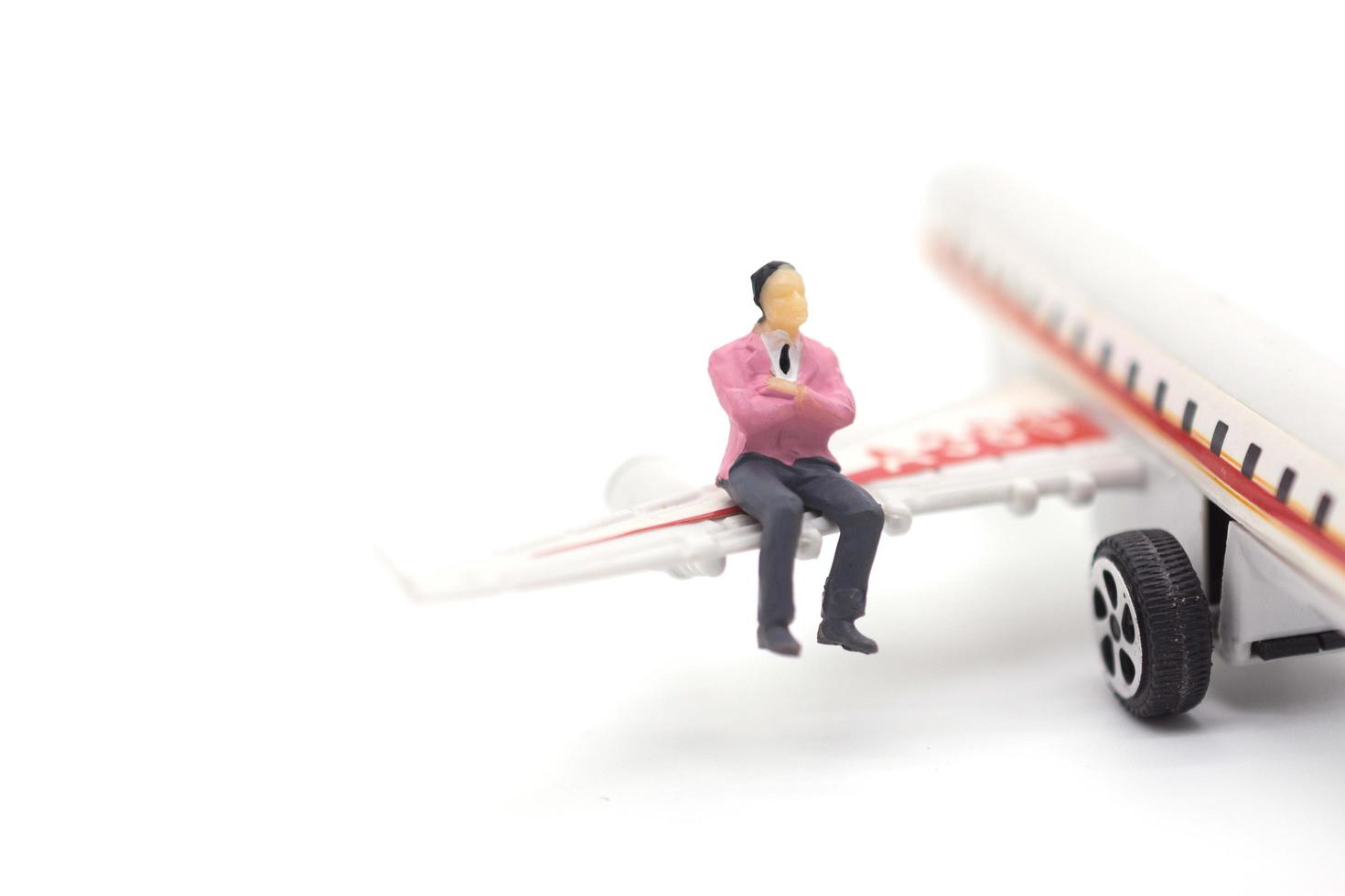 Miniature businessman sitting on airplane wing on white background photo