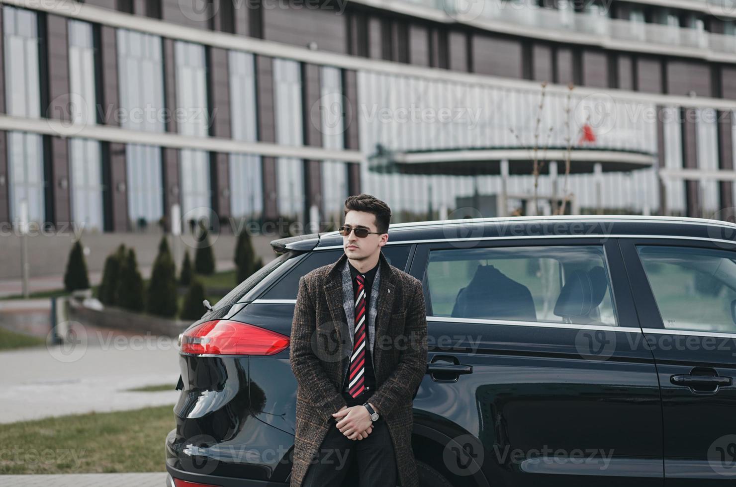handsome man in a coat stands next to a new car. photo