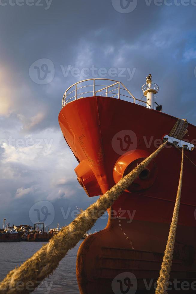 Low angle view of cargo ship docked at port against rain cloudy sky at sunset time in vertical frame photo