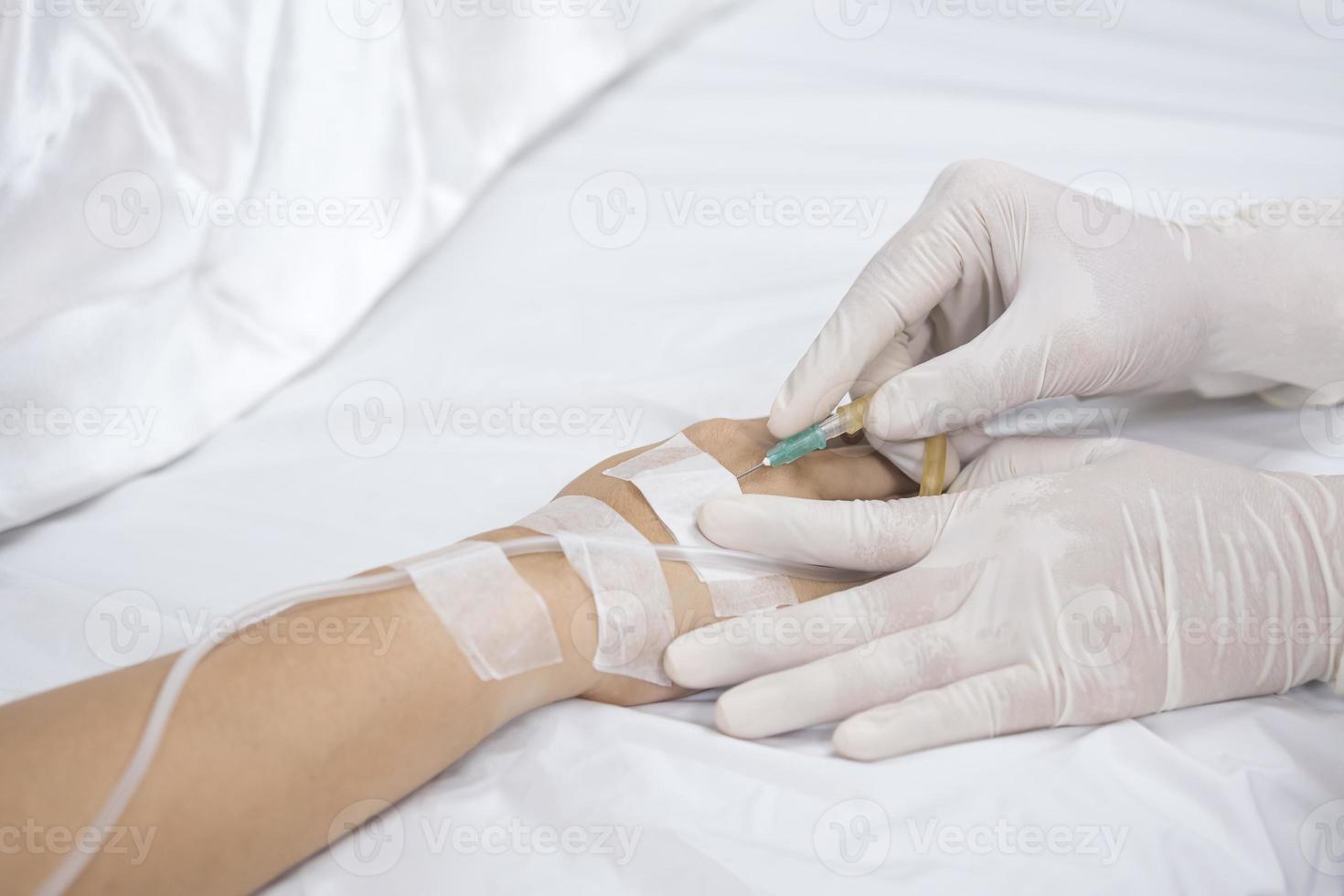 cerrar la mano del médico inyecta una aguja de infusión salina en el paciente en la cama foto
