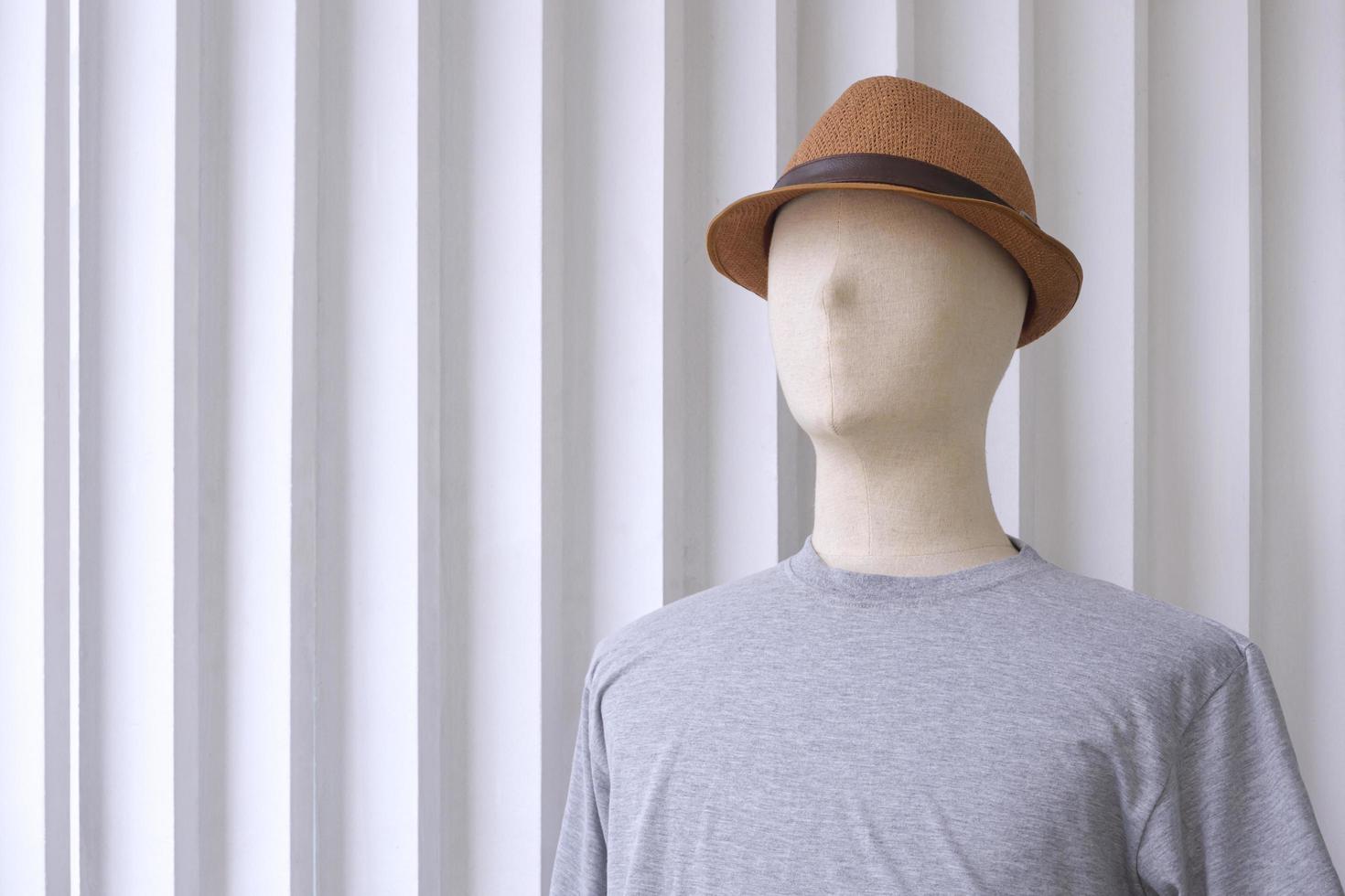 Male mannequin in gray t-shirt with fedora hat on white wooden wall background photo