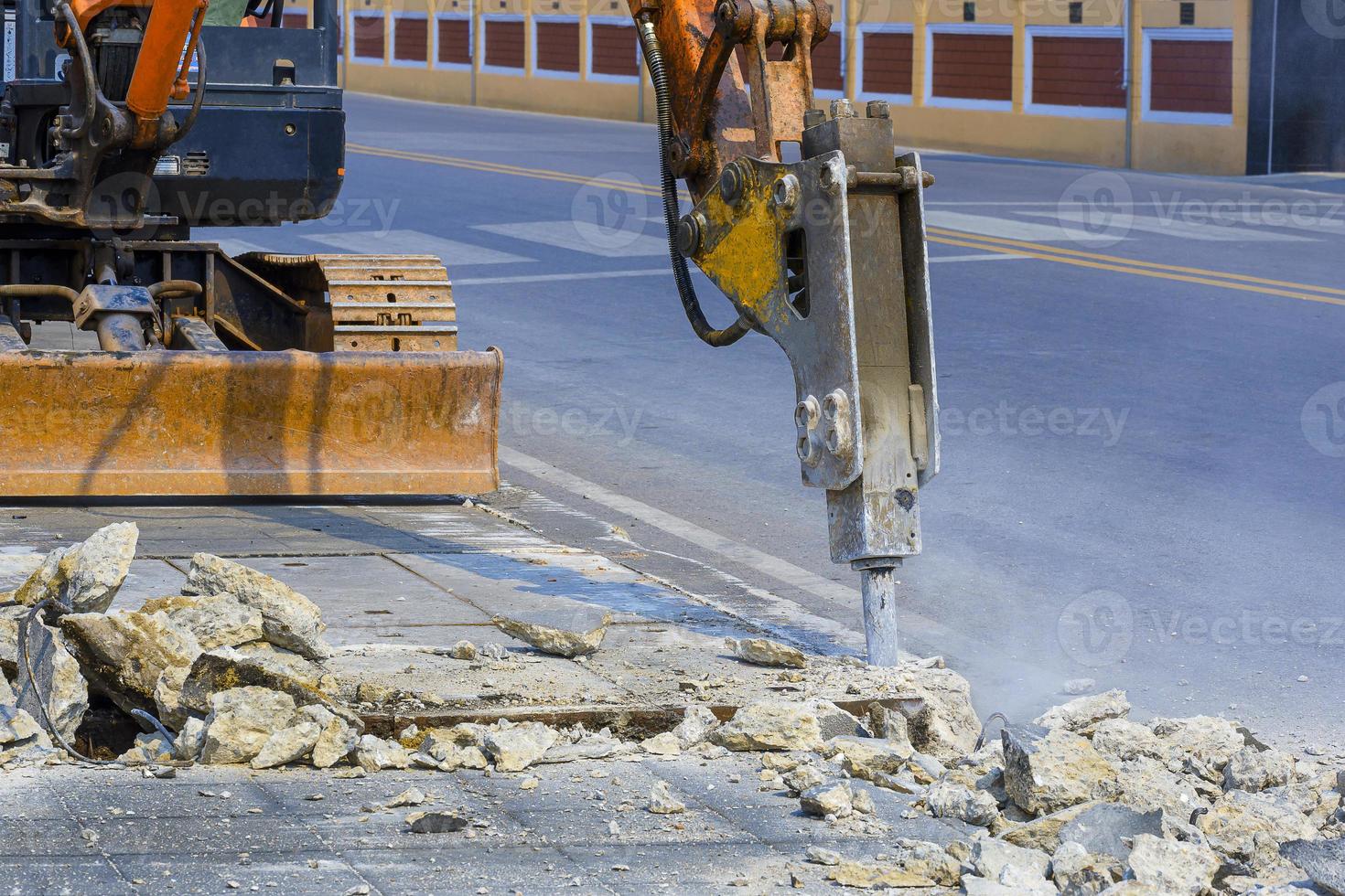 Selective focus of excavator hydraulic crushing hammer is breaking pavement on roadside area for preparing to install sewer system project photo