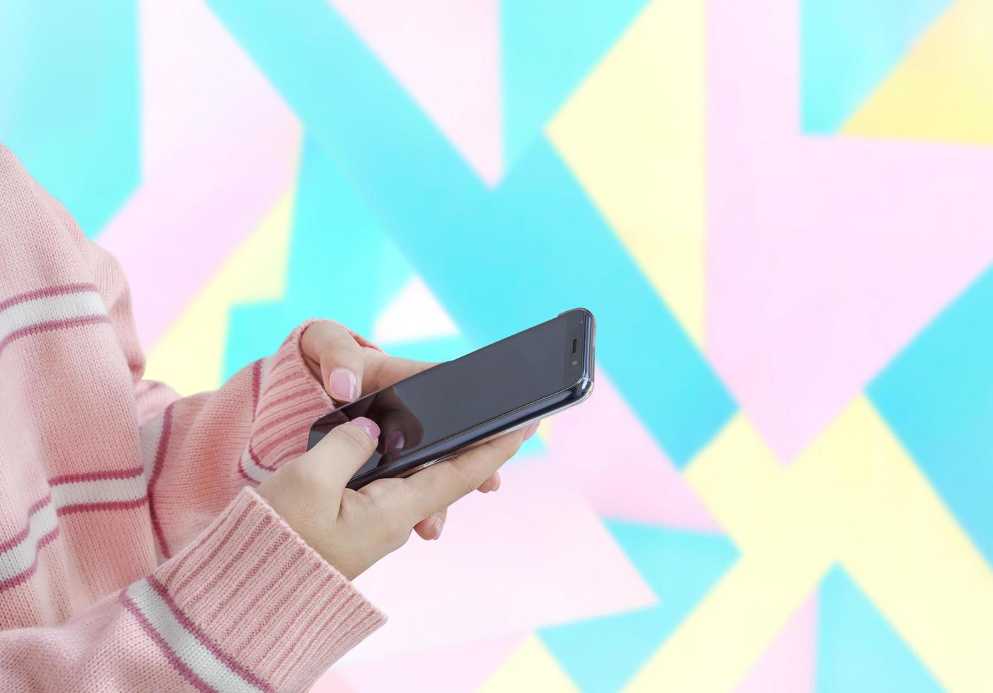 mano adolescente femenina en suéter rosa usando un teléfono inteligente en un fondo de pared pastel colorido foto