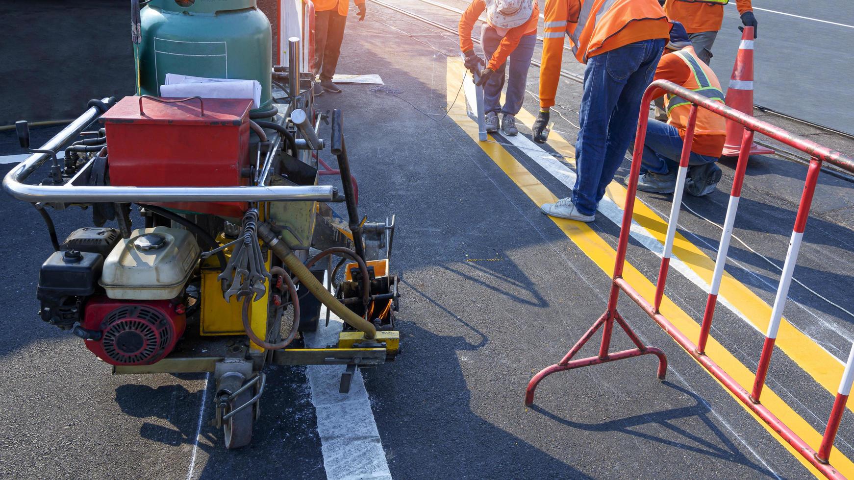 Road workers group with thermoplastic spray road marking machine are working to paint traffic lines on asphalt road with railway track crossing on street surface photo