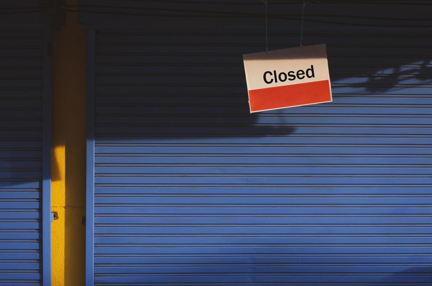 Hanging closed sign board in front of blue shutter door of grocery with sunlight and shadow on surface in vintage tone style photo