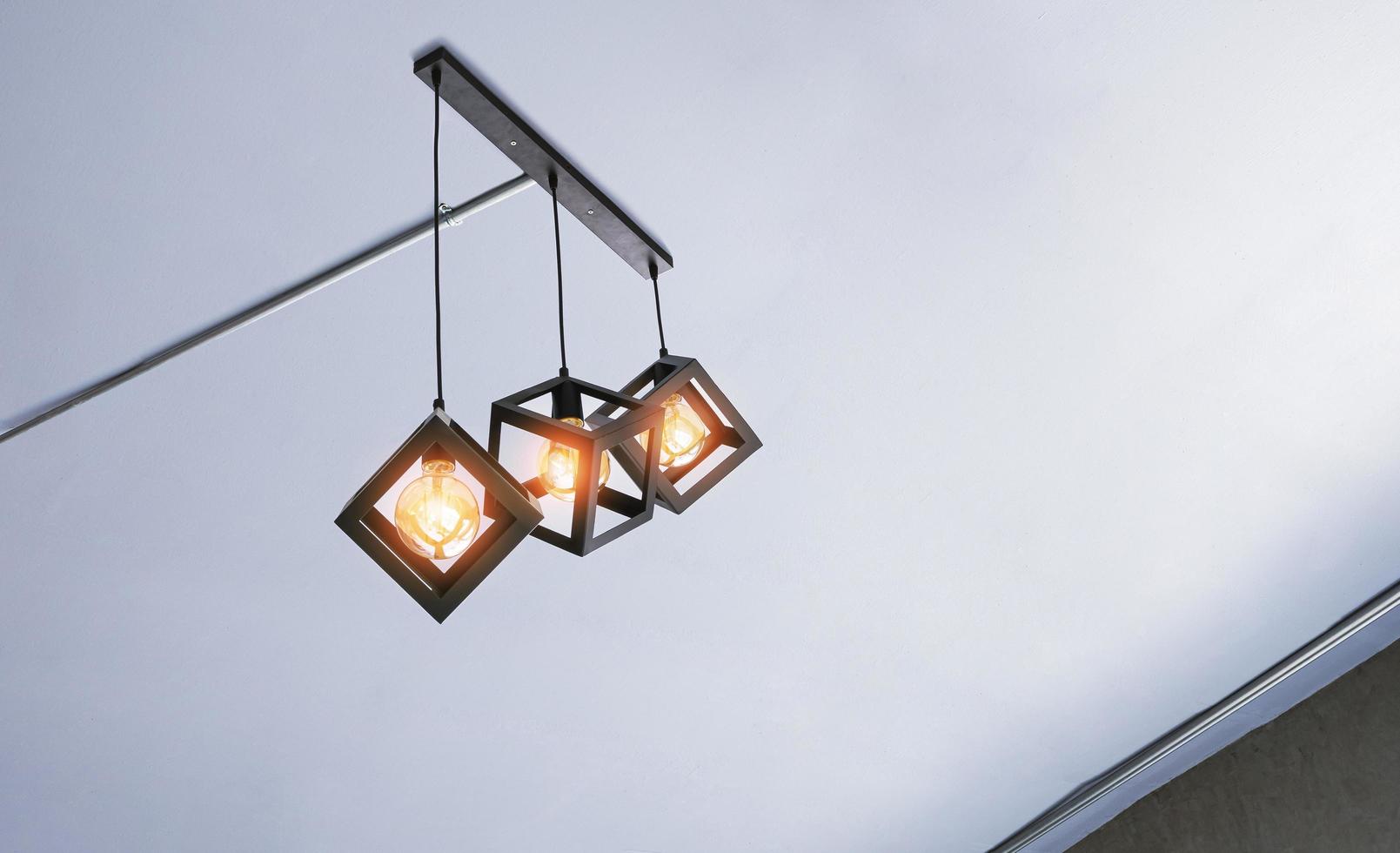 Low angle view of Illuminated modern three metal cage hanging lamps with electrical conduit pipes on white ceiling inside of living room photo