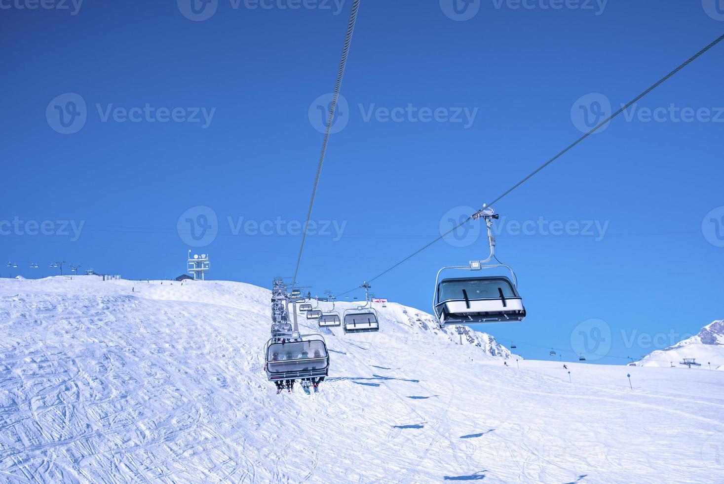 Ski lift moving over snow covered landscape against clear blue sky photo