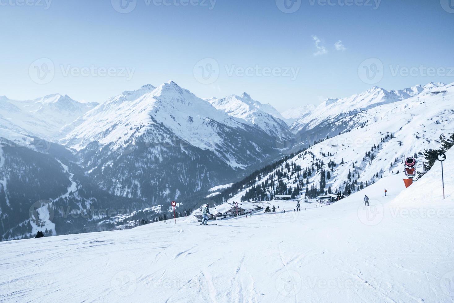 esquiadores esquiando en la ladera de una montaña cubierta de nieve contra el cielo azul foto