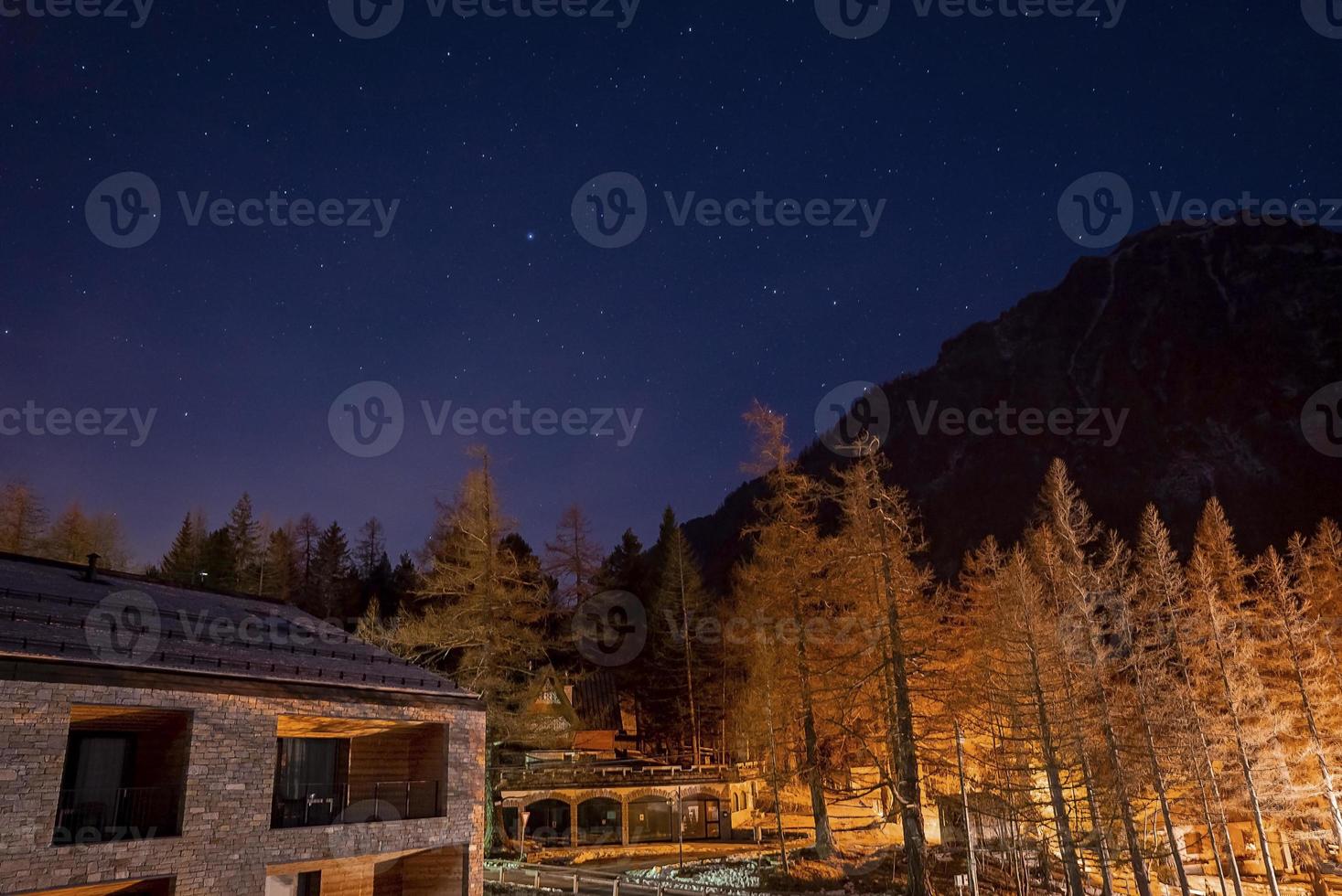 View of illuminated ski resort by pine trees and mountain during starry night photo