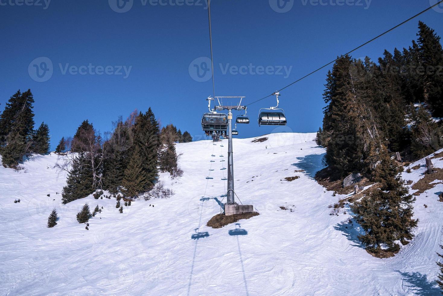 Ski lift passing amidst trees over snowy mountains photo