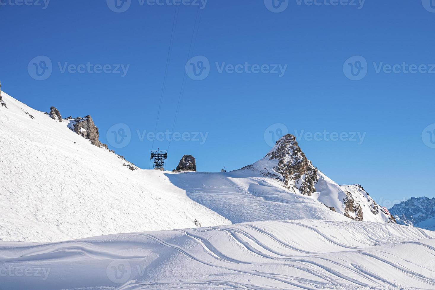 View of ski tracks on snowy mountain against clear blue sky photo