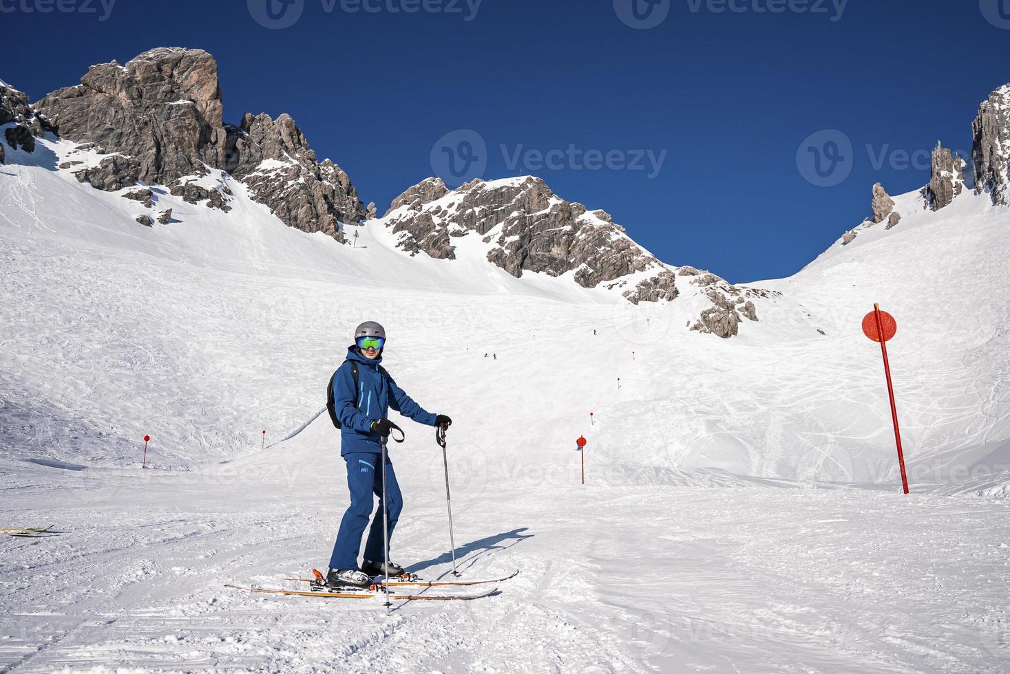Young skier with poles standing on snowy mountain slope at winter resort photo