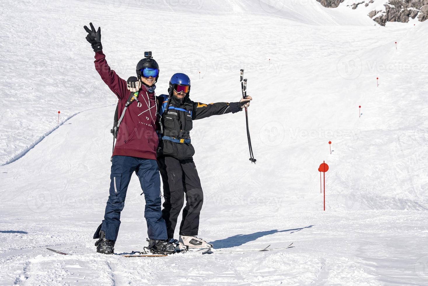 Snowboarder and skier with arms outstretched standing on mountain slope photo