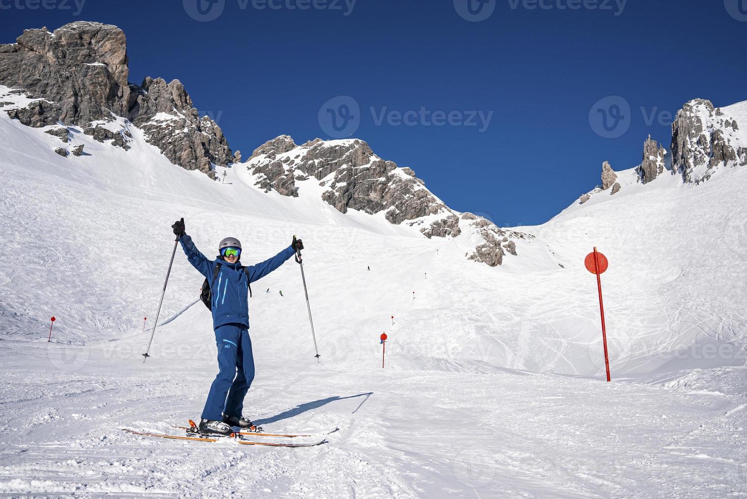 Skier holding poles with arms outstretched standing on snowy mountain slope photo