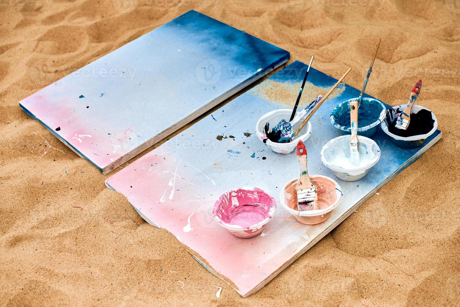 Two painted canvas with palettes of paints lying on sand, artist's palette at outdoor art festival photo