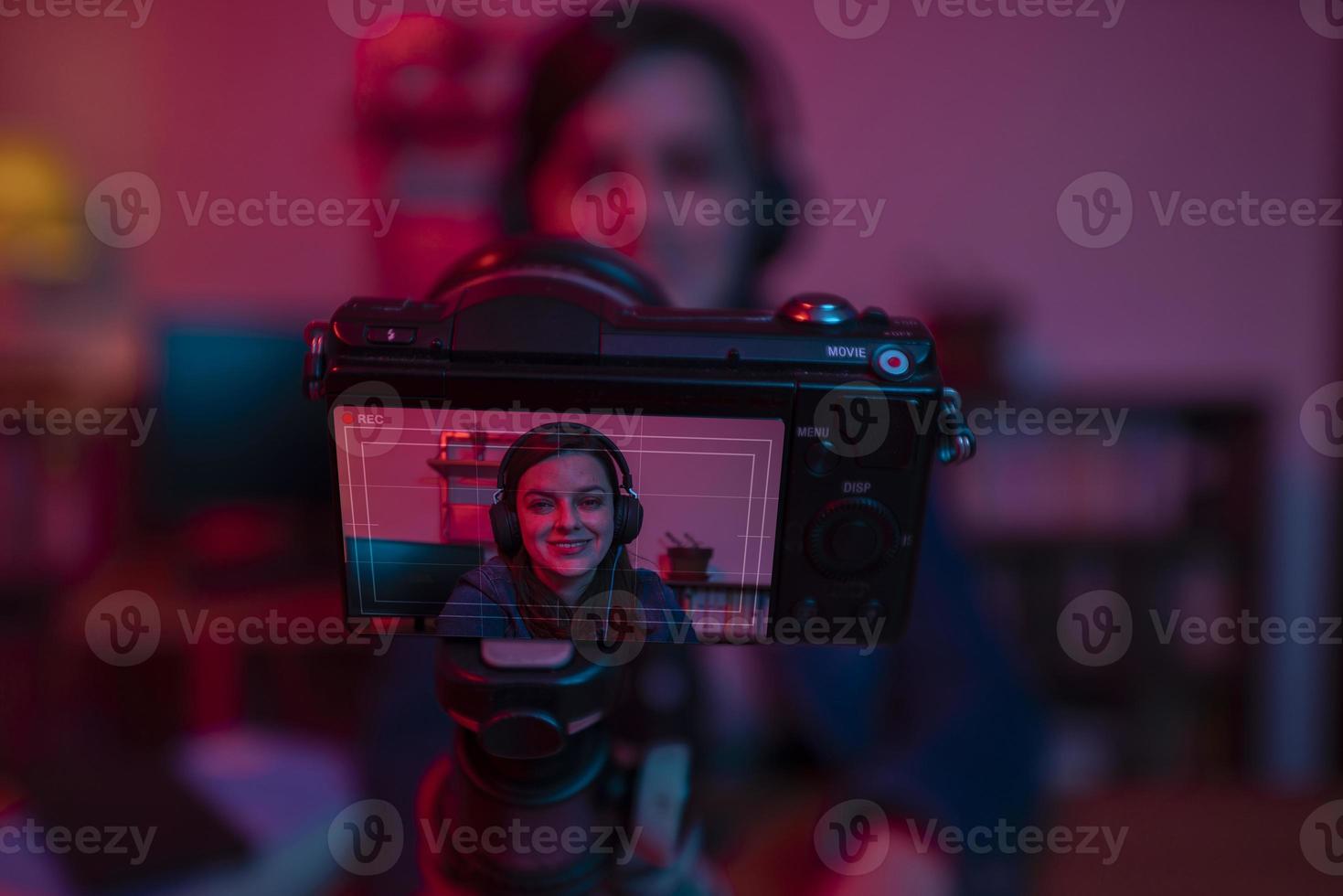 Beautiful Hispanic woman in front of a video camera recording a blog in her studio with red and blue lights inside her house photo