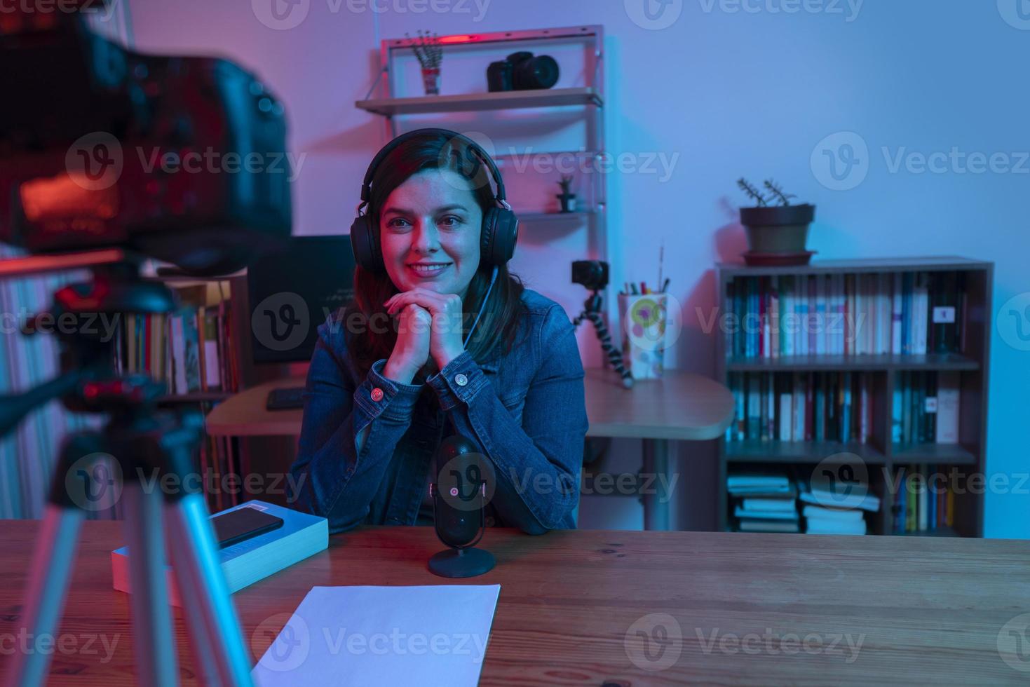 hermosa mujer hispana frente a una cámara de video grabando un blog en su estudio con luces rojas y azules dentro de su casa foto