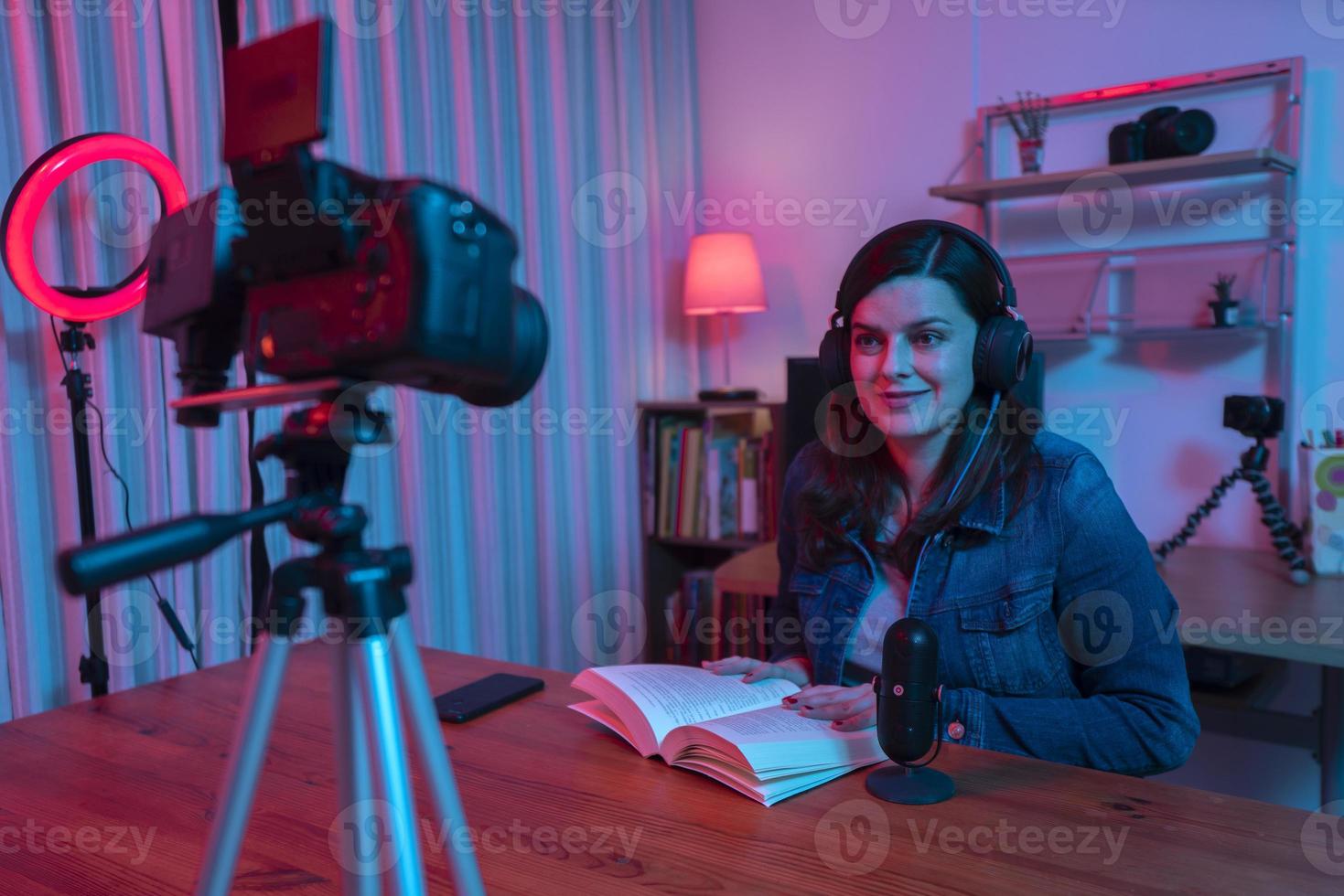 hermosa mujer hispana frente a una cámara de video grabando un blog en su estudio con luces rojas y azules dentro de su casa foto